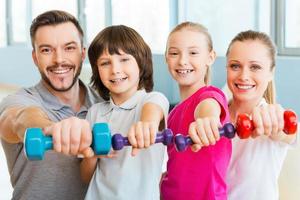 Living a healthy life together. Happy family holding different sports equipment while standing close to each other in health club photo