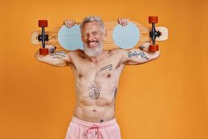 Shirtless senior man carrying skateboard on shoulders and smiling photo