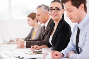 I love my job Side view of confident business people sitting in a row at the table while attractive woman looking at camera and smiling photo