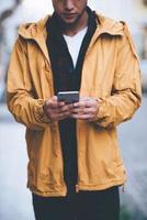 Typing message on the go. Close-up of handsome young man holding smart phone and looking at it while standing on the city street photo