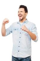 felicidad sin límites. feliz joven en camisa gesticulando y sonriendo mientras está de pie contra el fondo blanco foto