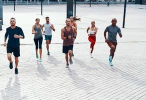 Full length of people in sports clothing jogging while exercising on the sidewalk outdoors photo