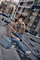 What if... Through the glass case view of thoughtful young woman in hat and coat looking away and smiling while spending time in the city photo