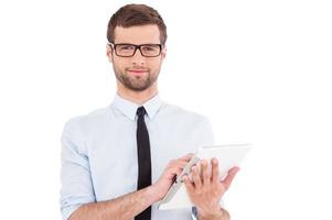 Expert in digital technologies. Cheerful young man in formalwear working on digital tablet and smiling while standing isolated on white background photo