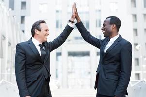 Business winners. Two cheerful business men clapping each other hands and smiling while standing outdoors photo