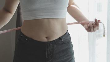 hermosa mujer gorda con cinta métrica usa su mano para exprimir el exceso de grasa que está aislado en un fondo blanco. ella quiere perder peso, el concepto de cirugía y descomponer grasa bajo el video