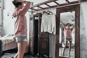 Everyday routine. Attractive young woman keeping hands in hair while standing in front of the mirror at home photo