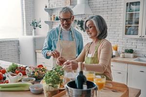 feliz pareja mayor en delantales preparando una cena saludable y sonriendo mientras pasa tiempo en casa foto