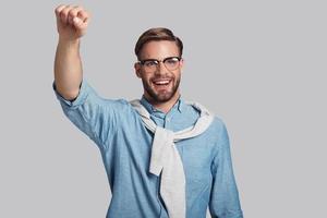 Achieving best results.  Good looking young man gesturing and smiling while standing against grey background photo