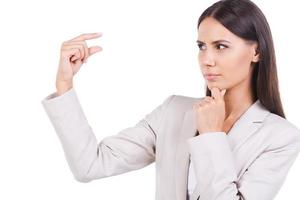 Too small. Beautiful young businesswoman in suit showing small size while standing against white background photo