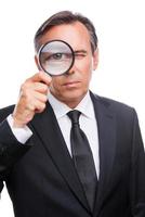 Businessman examining you. Serious mature man in formalwear examining you with magnifying glass while standing isolated on white background photo