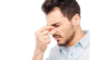 He is very tires today. Frustrated young man in shirt touching head and keeping eyes closed while standing against white background photo