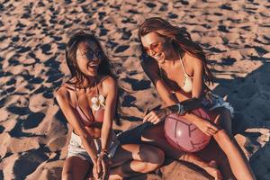 Total relaxation. Top view of attractive young women in swimwear smiling while sitting on the sand outdoors photo