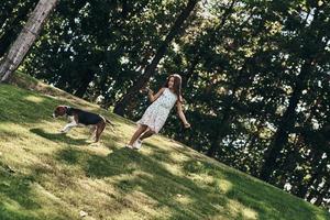 buscando aventuras juntos. toda la longitud de una linda niña jugando con su perro mientras corre al aire libre foto