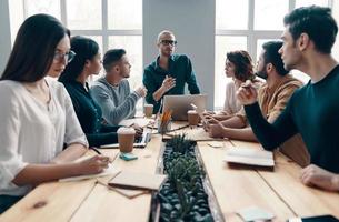 Discussing risky ideas. Group of young modern people in smart casual wear discussing something while working in the creative office photo