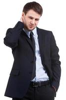 Feeling doubts. Frustrated young man in formalwear touching his neck and looking down while standing isolated on white photo