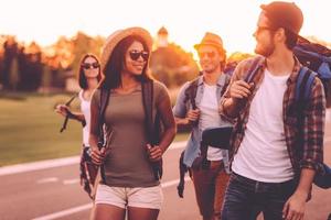 Having freedom to go anywhere. Group of young people with backpacks walking together by the road and looking happy photo