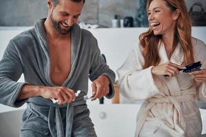 Loving young couple in bathrobes laughing while doing morning routine photo