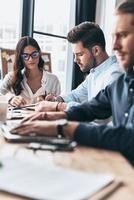 Achieving best results together. Young modern colleagues in smart casual wear working while spending time in the office photo