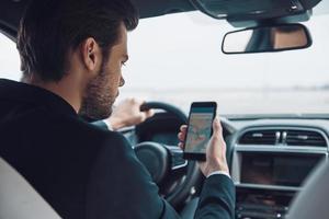 Where am I Rear view of young man in full suit using smart phone to check the map while driving a car photo