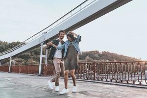 baile sin preocupaciones. toda la longitud de una pareja joven y juguetona tomándose de la mano y girando mientras bailan en el puente al aire libre foto