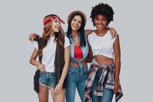 Three attractive stylish young women looking at camera and smiling while standing against grey background photo