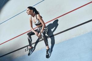 Resting after training. Top view of young woman in sports clothing resting while sitting on the running track outdoors photo