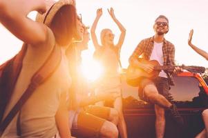 el mejor viaje por carretera jamás. grupo de jóvenes alegres bailando y tocando la guitarra mientras disfrutan juntos de su viaje por carretera en un camión de recogida foto