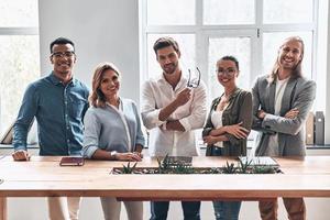 Happy business partners. Group of young modern people in smart casual wear looking at camera and smiling while standing in the creative office photo