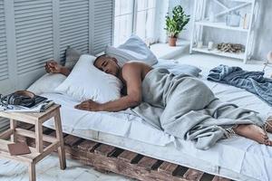 buen descanso. vista superior del joven africano durmiendo mientras está acostado en la cama en casa foto