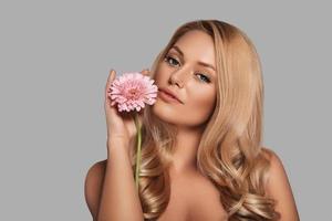 Sensual young woman looking at camera and holding a flower while standing against grey background photo