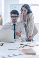 We have some problems with our statistics Young handsome man in glasses pointing at his laptop and discussing something with his beautiful coworker while sitting at the office table photo