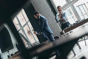 Fits perfect. Young fashionable designer showing his client stylish suit while standing in his workshop photo