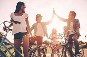 estamos listos para montar una vista de ángulo bajo de jóvenes alegres parados cerca de sus bicicletas en la carretera mientras dos hombres chocan los cinco foto