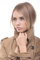 Feeling warm and trendy. Attractive young woman in coat covering her neck with collar and looking away while standing against white background photo