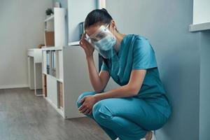 Tired young female nurse in protective workwear touching her head while working in the hospital photo