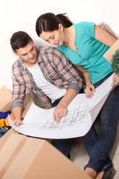 Planning a house improvement. Top view of young couple sitting on the floor and looking at the blueprint while cardboard boxes laying around them photo