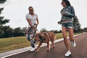 joven y lleno de energía. toda la longitud de una hermosa pareja joven corriendo con su perro mientras pasa tiempo al aire libre foto