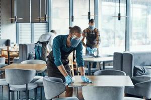 Three young male waiters in protective workwear cleaning tables for clients in restaurant photo