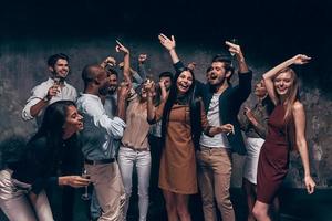 disfrutando de una fiesta increíble. grupo de hermosos jóvenes bailando con flautas de champán y luciendo felices foto