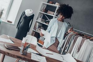 Searching for fashion muse. Serious young African woman holding eyeglasses and looking at paper while standing in her studio photo