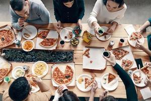 Best dinner. Top view of young people in casual wear picking pizza while having a dinner party indoors photo