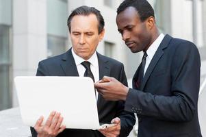 Discussing a new project. Two confident business men looking at laptop while one of them pointing it with finger photo