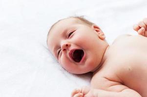 Crying baby. Top view of little baby lying in bed and crying photo