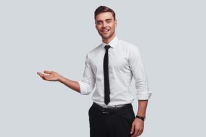 Over here Good looking young man pointing copy space and smiling while standing against grey background photo