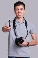 cuidar de su lente joven alegre en camisa de polo sosteniendo una cámara digital y estirando el cepillo de la lente mientras está de pie en el estudio foto