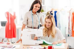 Working on new fashion styles. Two happy young women sewing together in their fashion workshop photo