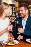 Cheers to us Beautiful young loving couple toasting with red wine and smiling while sitting at the restaurant together photo