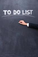 To do list. Close-up of human hand writing to do list on the blackboard photo