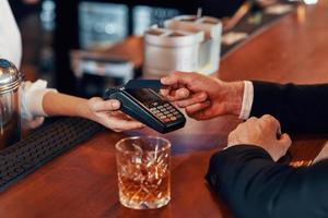 Top view close-up of man making a contactless payment while sitting at the bar counter in restaurant photo